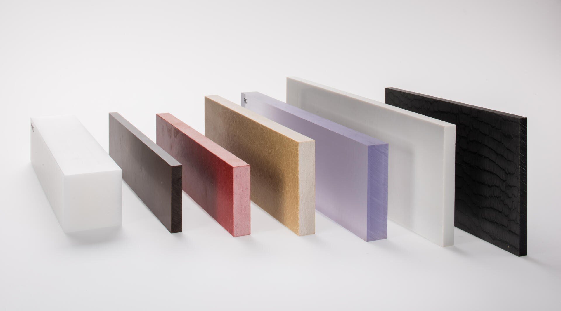 Sieben rechteckige Platten in verschiedenen Farben und Strukturen, darunter weiß, schwarz, rot, beige, lila und klar, sind aufrecht in einer diagonalen Reihe vor einem weißen Hintergrund angeordnet.