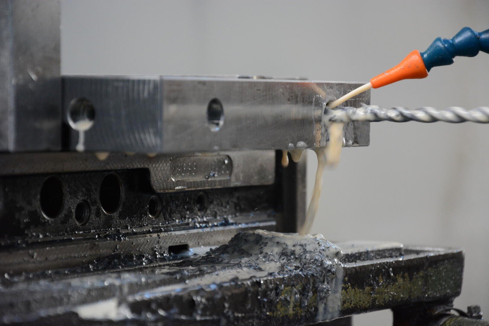 Gros plan d'une machine d'usinage des métaux perçant une pièce métallique, un liquide de refroidissement étant appliqué par une buse pour refroidir et lubrifier le processus de perçage.