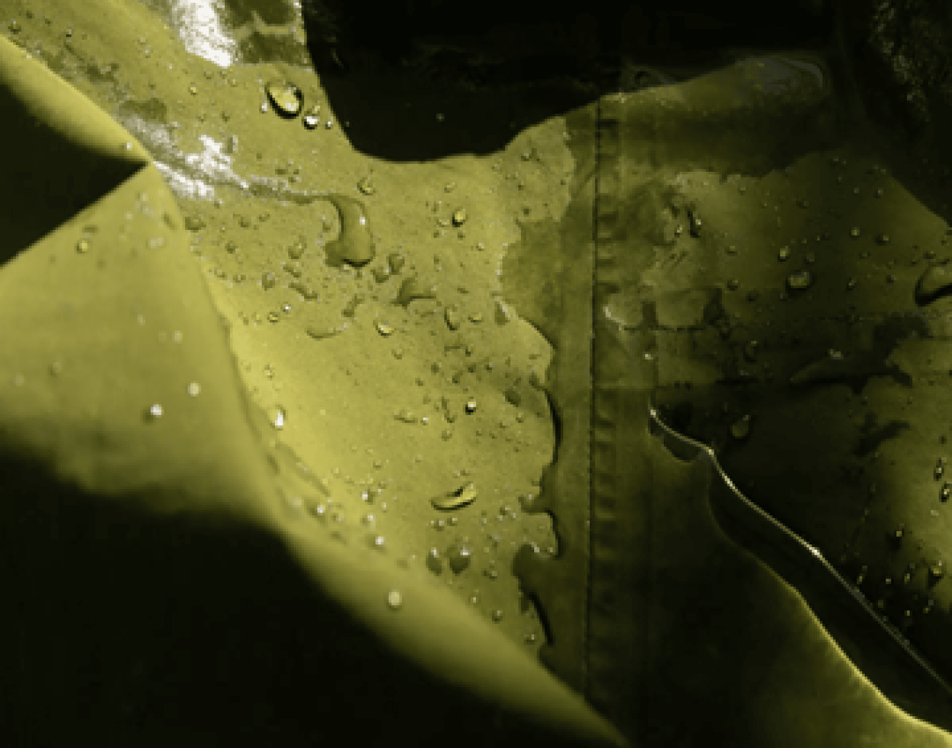 Nahaufnahme von Wassertropfen auf einem grünen, wasserdichten Stoff, wobei das Sonnenlicht Schatten und Lichter auf die Oberfläche wirft.
