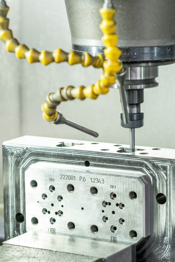 Gros plan sur une fraiseuse CNC usinant un bloc de métal, avec des tuyaux de refroidissement flexibles jaunes à proximité de l'outil de tournage.