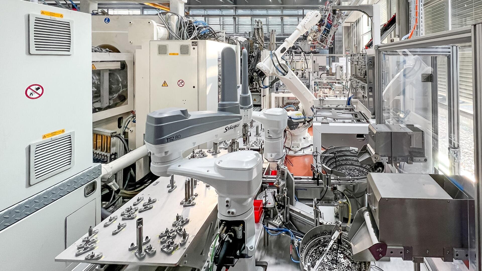 Un intérieur d'usine moderne avec des bras robotisés et des machines automatisées qui assemblent des pièces sur une chaîne de production, entouré d'appareils métalliques et de composants électroniques.