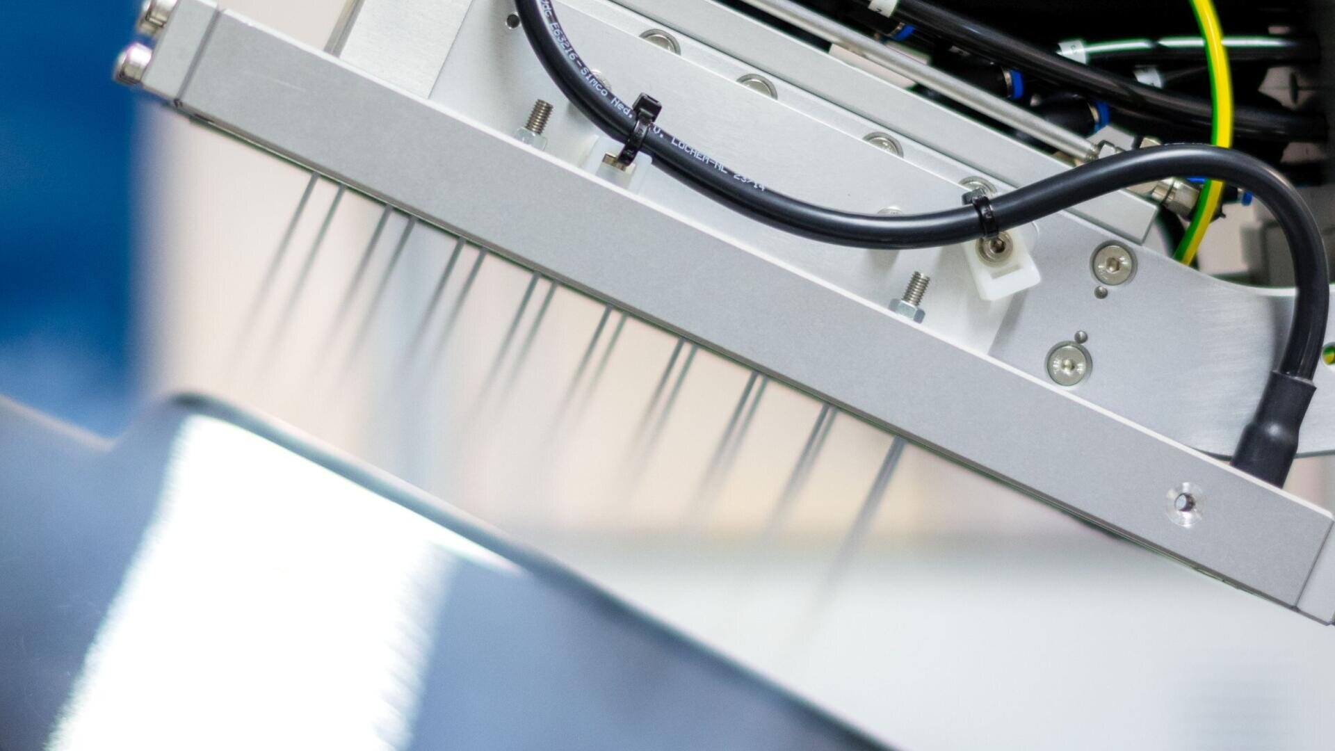 Gros plan sur une machine robotisée équipée de plusieurs buses métalliques en forme d'aiguilles, qui font probablement partie d'un processus industriel ou de laboratoire automatisé, et qui sont fixées à un composant métallique et électronique.