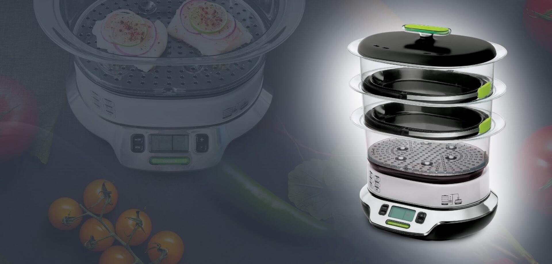 Ein dreistufiger digitaler Dampfgarer mit einem Display und grünen Akzenten, dargestellt auf einem dunklen Hintergrund, auf dem Tomaten und Gemüse teilweise sichtbar sind.