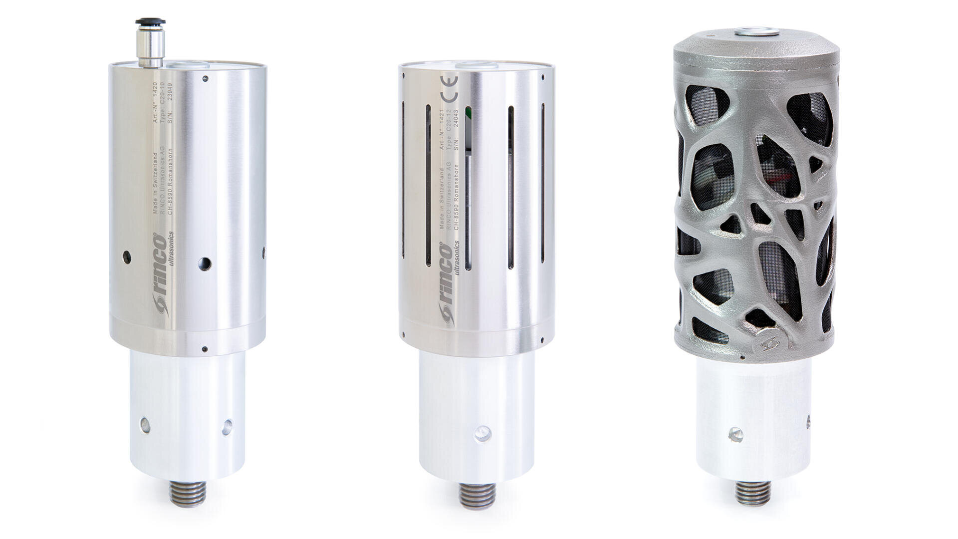 Drei zylindrische, metallische Industriewerkzeuge oder Bauteile, zwei mit glatter, silberner Oberfläche und technischer Beschriftung und eines mit einer Außenschicht, die auf der rechten Seite ein kompliziertes, gitterartiges Muster aufweist. Alle Teile sind mit einem Gewinde versehen.