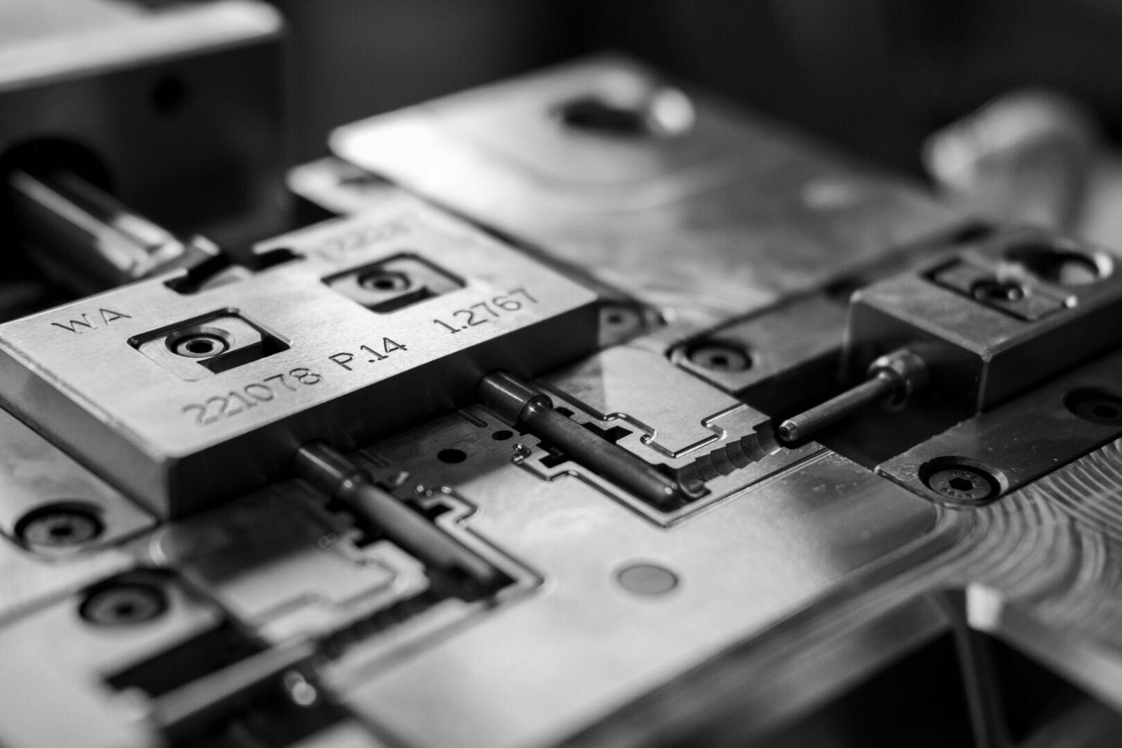 Gros plan sur un moule ou une matrice métallique de précision avec des chiffres et des lettres gravés, présentant des formes géométriques complexes et des détails mécaniques en noir et blanc.