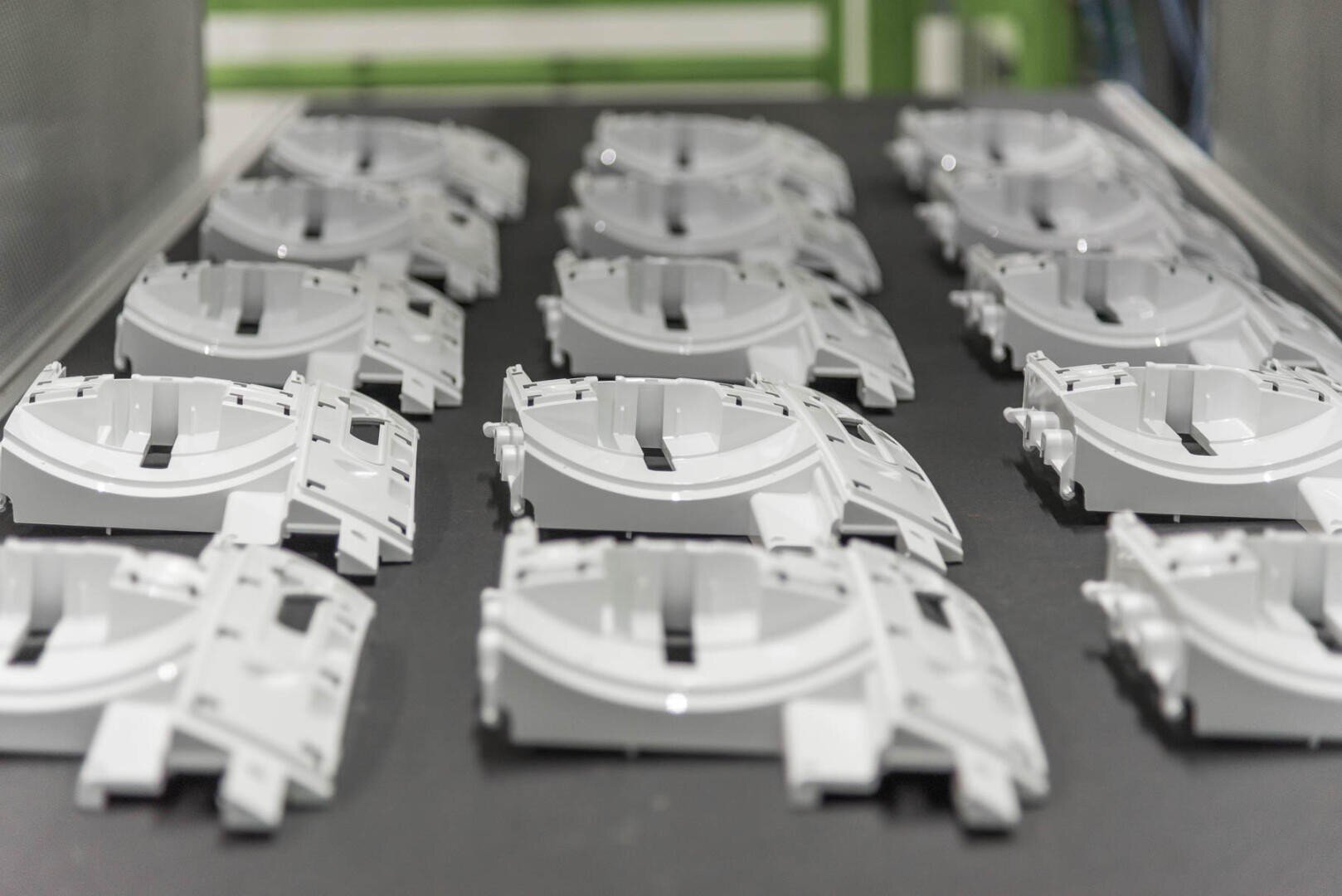 Reihen identischer weißer Kunststoffteile sind ordentlich auf einem schwarzen Förderband in einer Fabrik oder Produktionsstätte angeordnet.