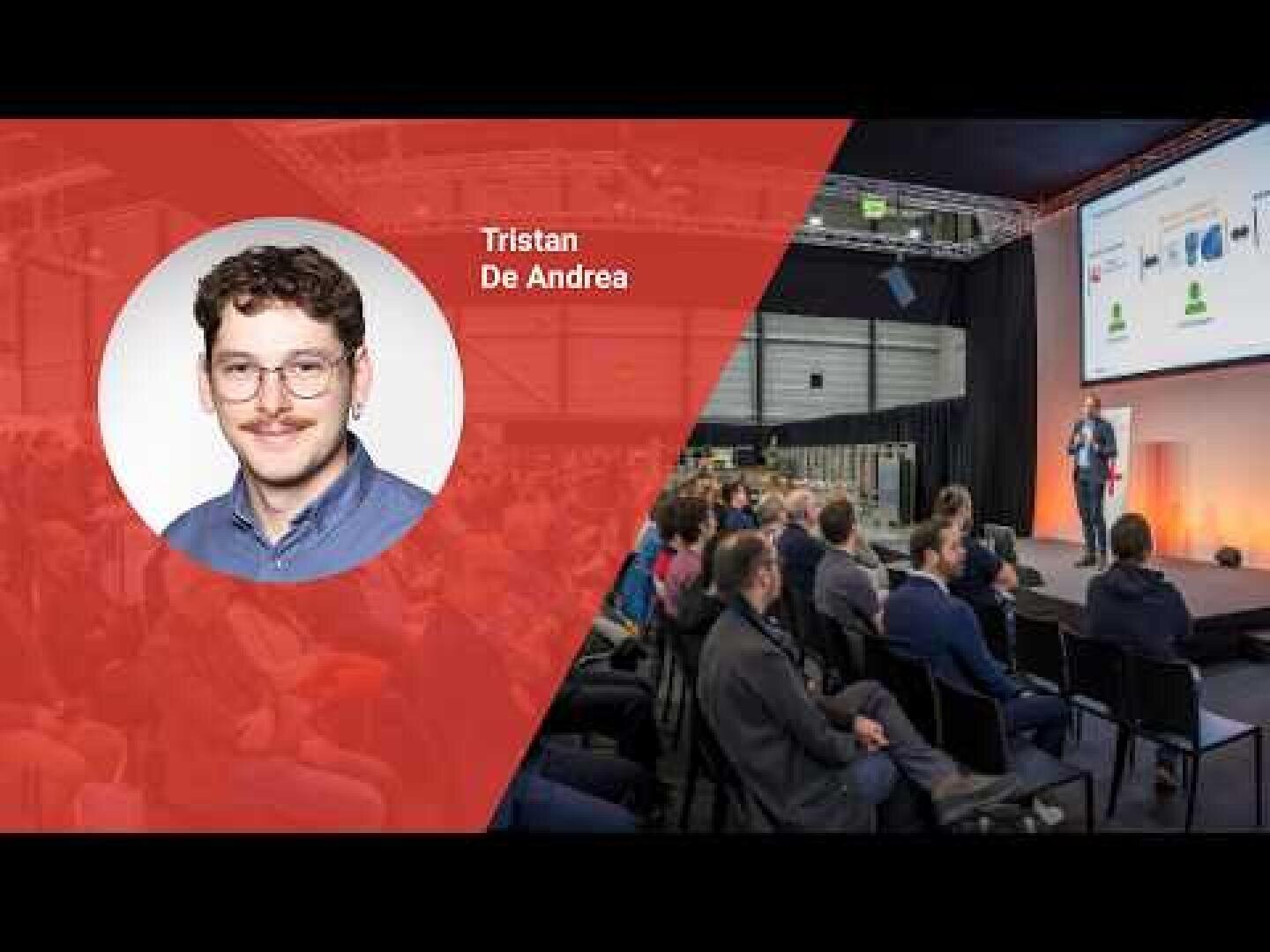 Das Porträt eines Mannes mit der Aufschrift "Tristan De Andrea" ist auf einem roten Overlay zu sehen, während das Publikum einem Redner zusieht, der auf der Bühne eines modernen Konferenzraums Folien präsentiert.