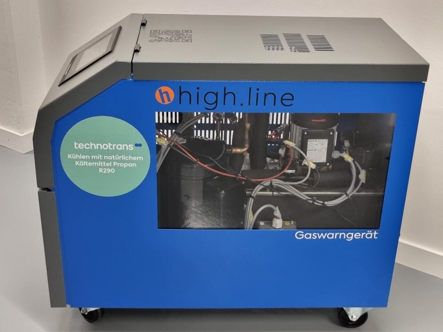 Eine blaue Industriemaschine mit der Aufschrift high.line und technotrans mit einem Fenster, durch das die inneren Komponenten sichtbar sind. Sie ist mit einem Schild versehen, das auf die Verwendung des natürlichen Kältemittels Propan R290 hinweist, und trägt die Aufschrift "Gaswarngerät".