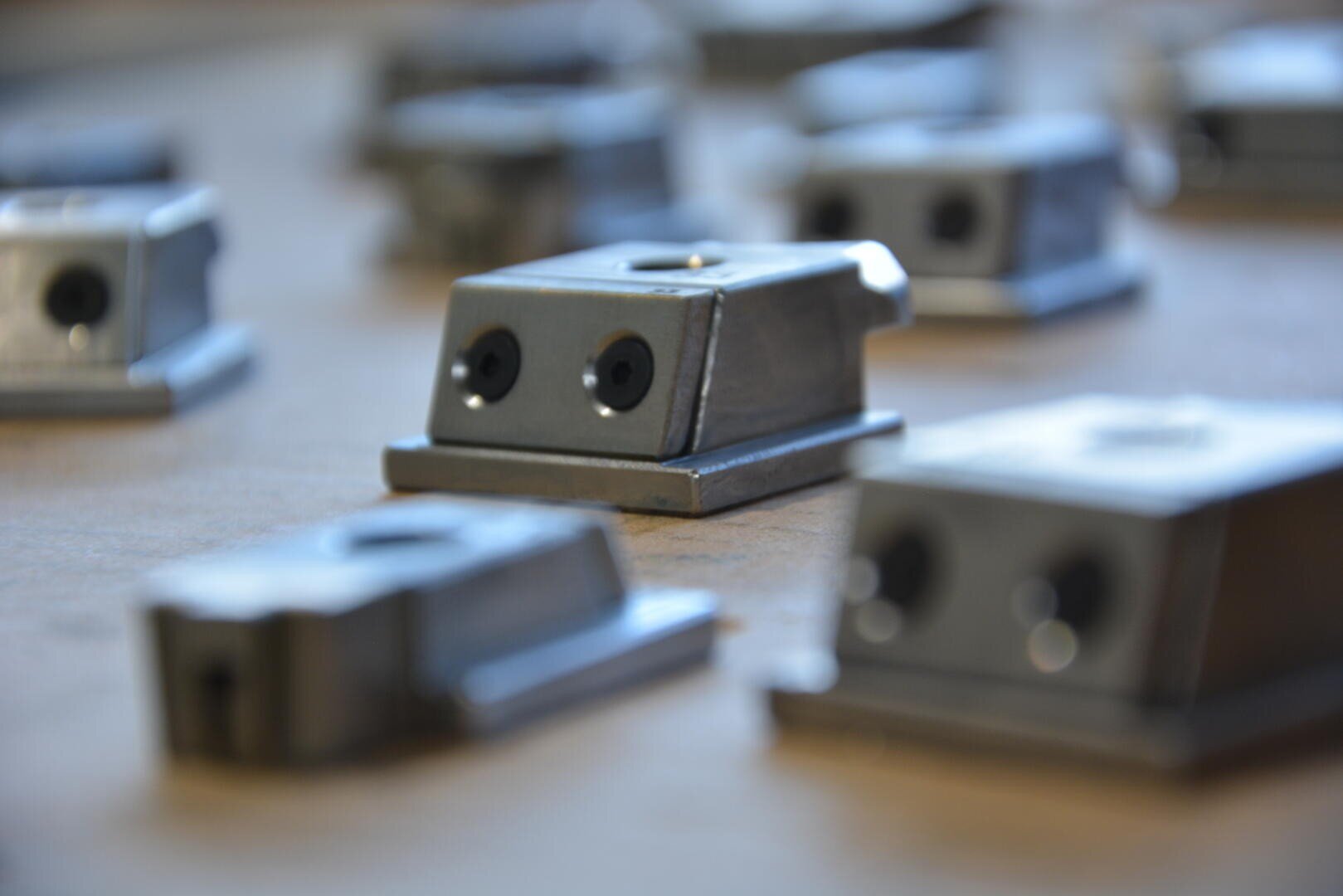 Plusieurs petits objets métalliques rectangulaires percés de deux trous circulaires sont disposés sur une surface plane. La faible profondeur de champ fait qu'un seul objet au centre apparaît net et mis au point.