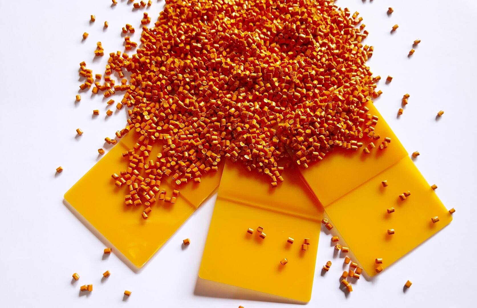Ein Haufen kleiner orangefarbener Kunststoffkügelchen, verteilt auf vier rechteckige gelbe Kunststoffmuster auf weissem Hintergrund.