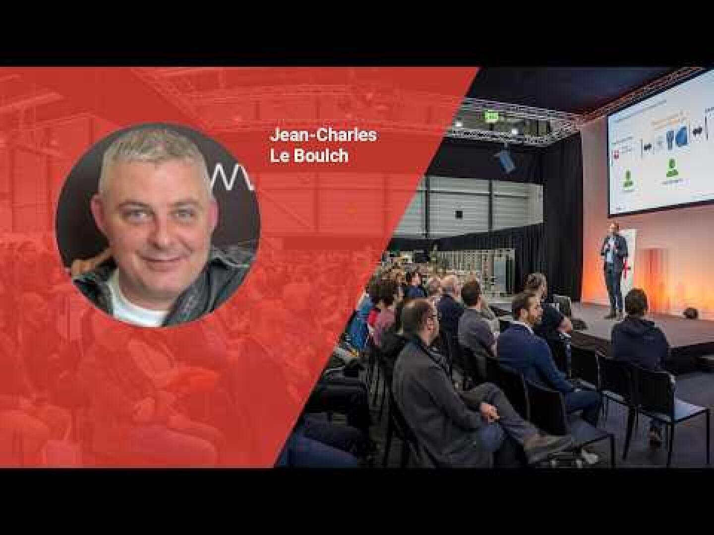 Ein Mann spricht auf der Bühne zu einem Publikum in einem großen Saal. Auf der linken Seite zeigt eine rote Grafik den Kopf eines Mannes namens Jean-Charles Le Boulch. Das Publikum sitzt und schaut sich die Präsentation an.