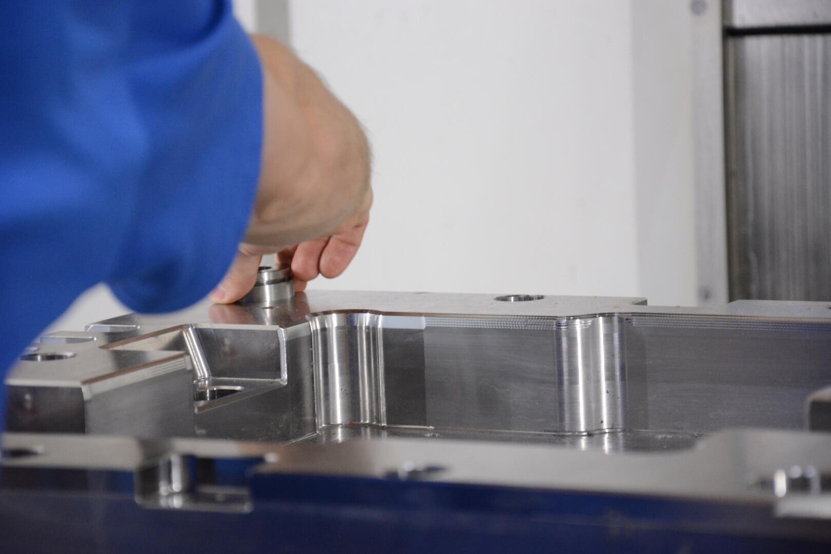 Une personne vêtue d'un manchon bleu ajuste ou inspecte une grande pièce métallique brillante d'une machine, peut-être au cours d'un processus de fabrication ou d'assemblage.