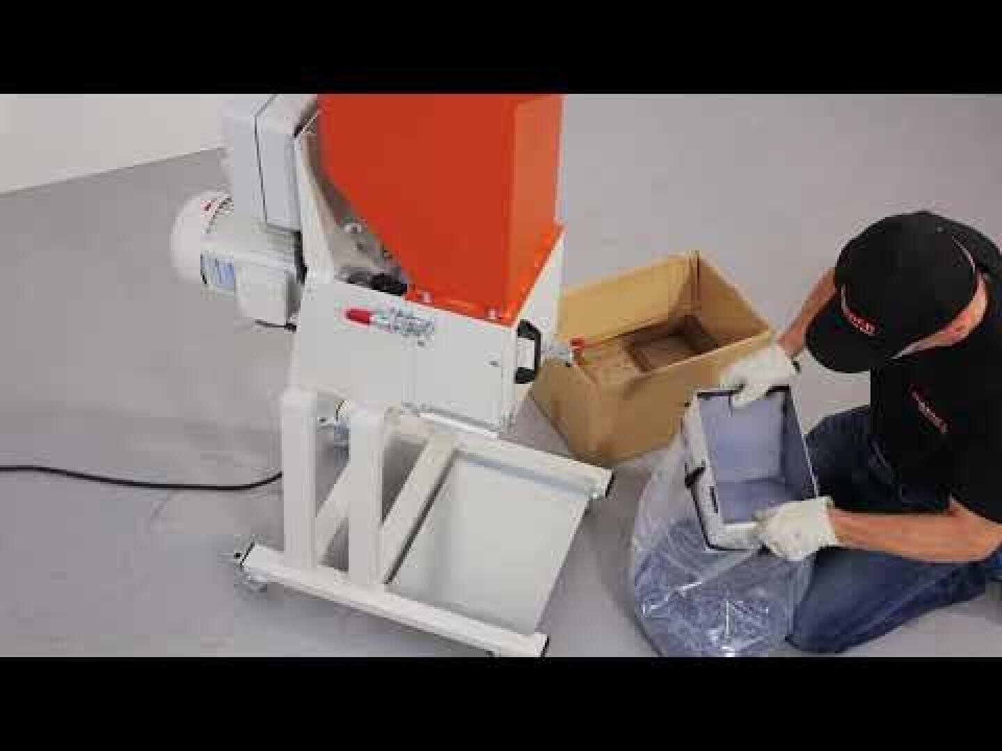 Une personne portant des gants est accroupie à côté d'une petite déchiqueteuse industrielle et manipule des matériaux déchiquetés qu'elle place dans un sac en plastique à côté d'un carton.