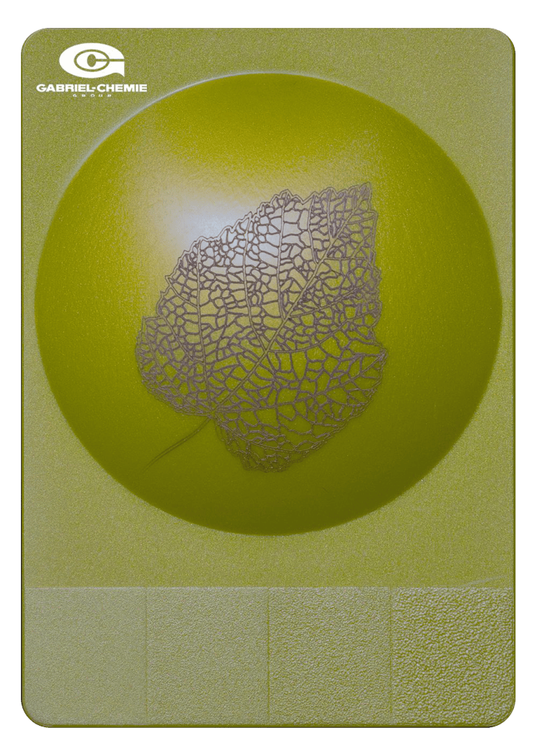 Auf der metallisch gelben Oberfläche befindet sich ein erhabener kreisförmiger Bereich mit einem detaillierten, spitzenartigen Blattmuster in der Mitte. Das Gabriel-Chemie-Logo erscheint in der oberen linken Ecke. Im unteren Bereich sind strukturierte Blöcke abgebildet.