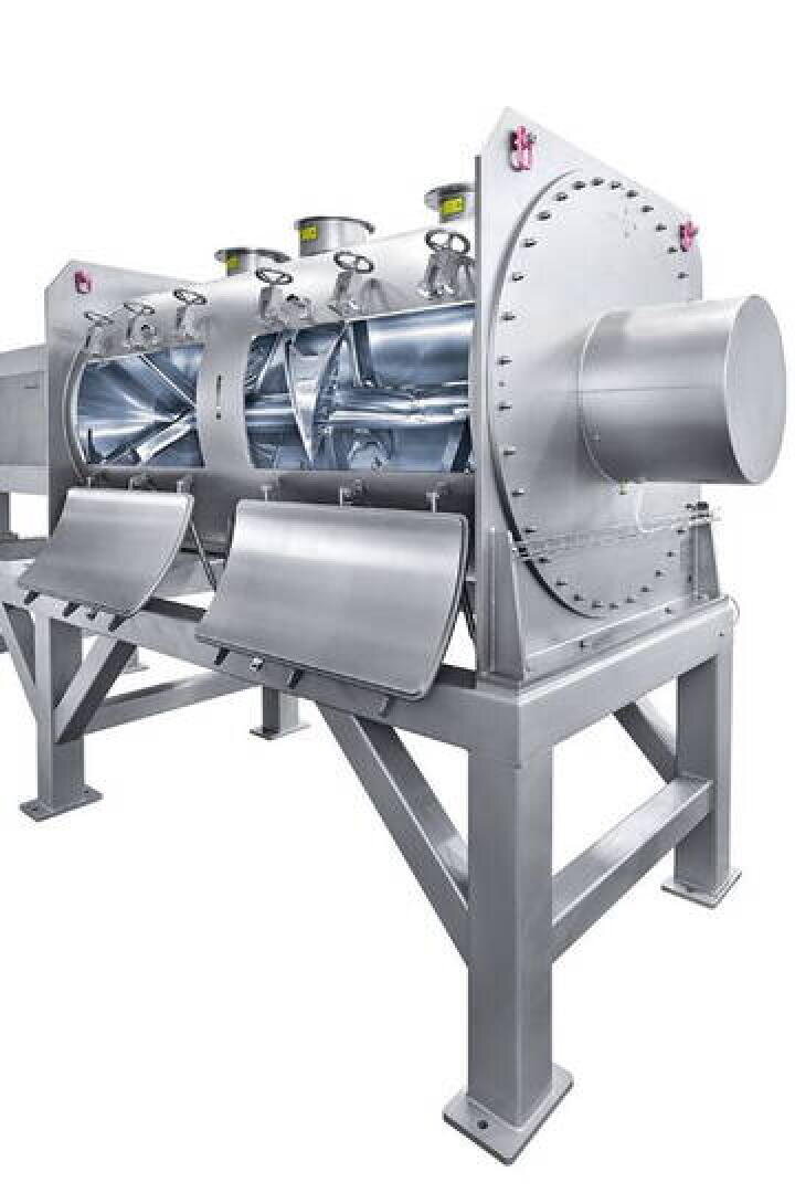 Un grand mélangeur industriel en acier inoxydable avec des portes d'inspection ouvertes montre ses pales rotatives internes et sa structure cylindrique robuste, soutenue par un cadre métallique solide.