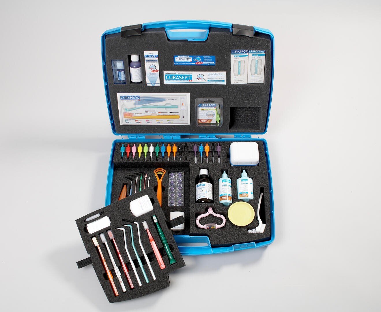 Ein blauer Koffer öffnete sich und enthüllte verschiedene Zahnpflegehilfsmittel wie Zahnbürsten, Interdentalbürsten, Flaschen, Dosen und Zahnpflegeprodukte, die alle übersichtlich in speziellen Schaumstofffächern angeordnet waren.