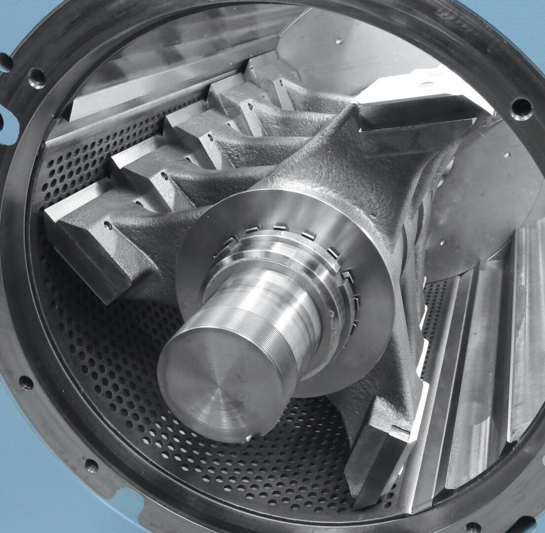 Gros plan sur une grande pièce de machine industrielle métallique avec des composants complexes et anguleux et un centre cylindrique situé dans une chambre métallique perforée.