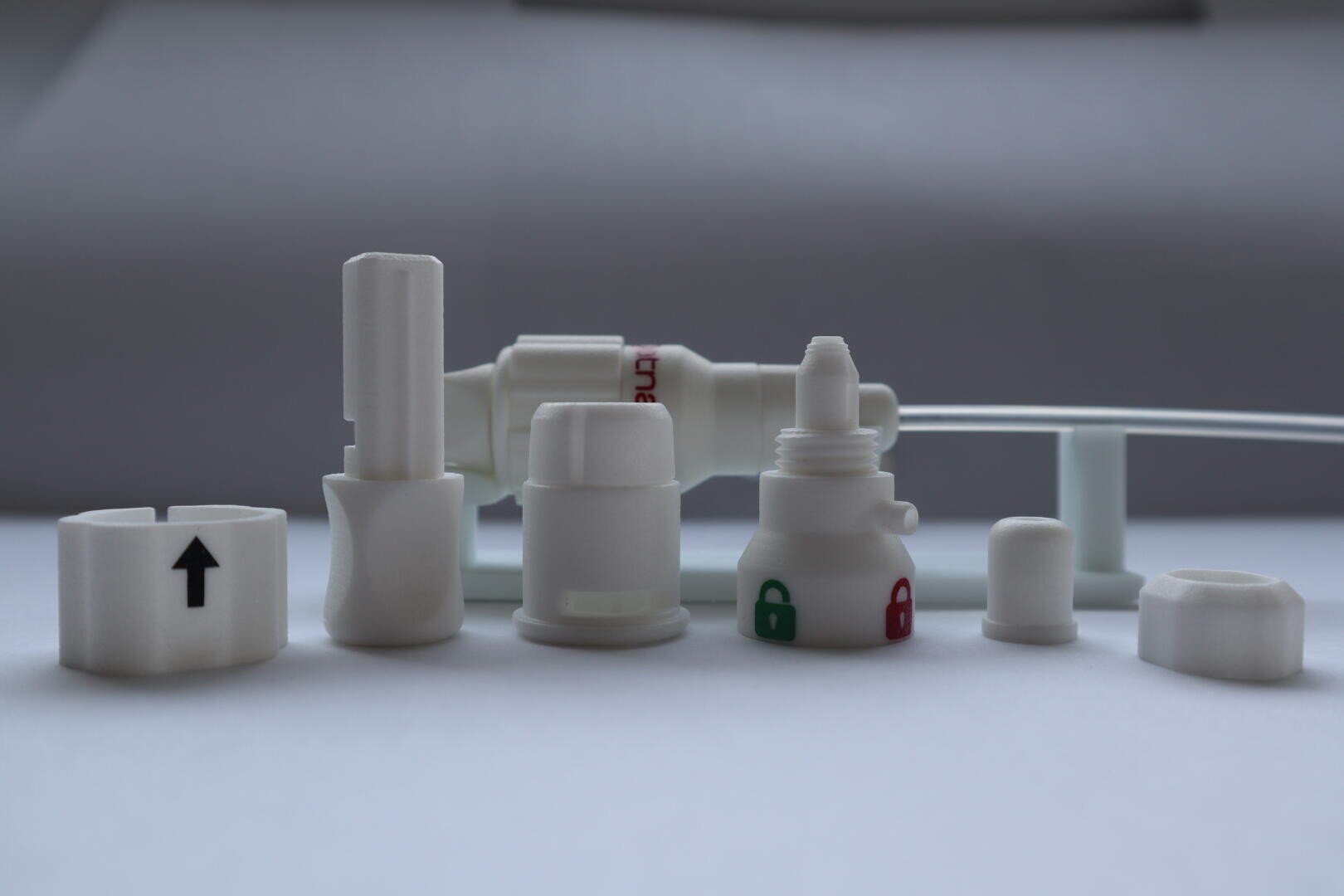 Une série de composants en plastique blanc pour les appareils médicaux, y compris des connecteurs et des capuchons, représentés sur un fond neutre. Certains ont des flèches ou des symboles de cadenas en noir, vert et rouge indiquant des directions ou des fonctions.