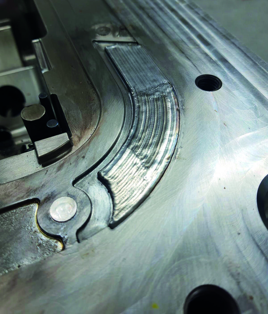 Gros plan sur une pièce de machine métallique avec des soudures et des rainures visibles sur la surface, montrant une zone qui semble avoir été récemment réparée ou modifiée.