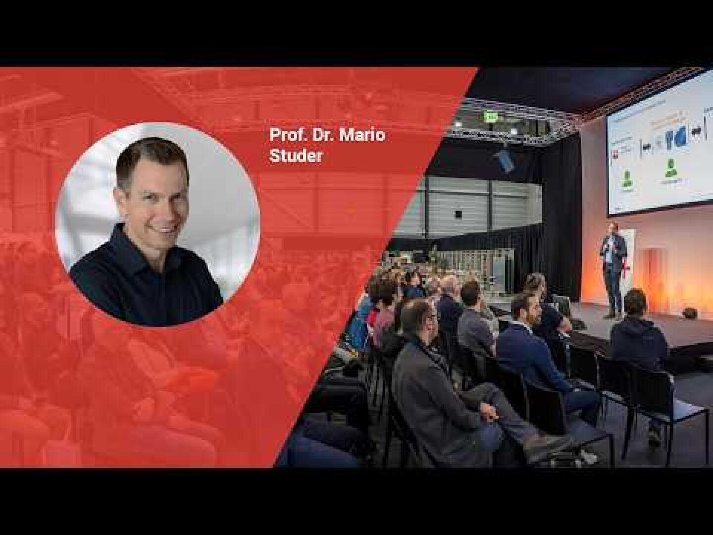 Ein grosses Publikum sitzt in einem modernen Konferenzsaal und beobachtet einen Mann, der auf der Bühne einen Vortrag hält. Auf der linken Seite befindet sich ein rotes Overlay mit dem Kopfbild eines lächelnden Mannes mit der Aufschrift Prof. Dr. Mario Studer.