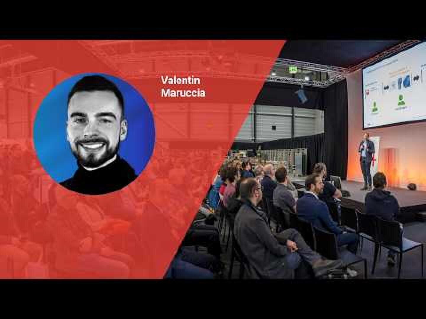 Ein Redner spricht auf der Bühne vor einem Publikum in einem Konferenzraum. Auf der linken Seite zeigt ein rotes Grafik-Overlay ein Kopfbild und den Namen Valentin Maruccia. Das Publikum sieht den Redner und die Präsentationsfolien.