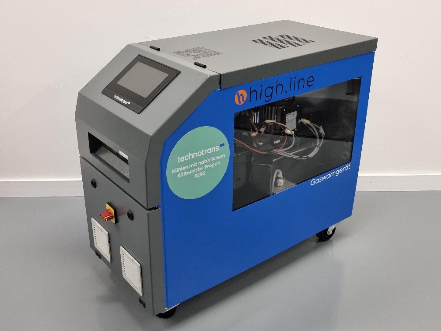 Eine graue und blaue Industriemaschine mit einem Touchscreen, beschriftet mit high.line, mit einem Seitenfenster, das interne Komponenten zeigt. Die Maschine steht auf Rädern und hat Etiketten und Schalter an der Außenseite.