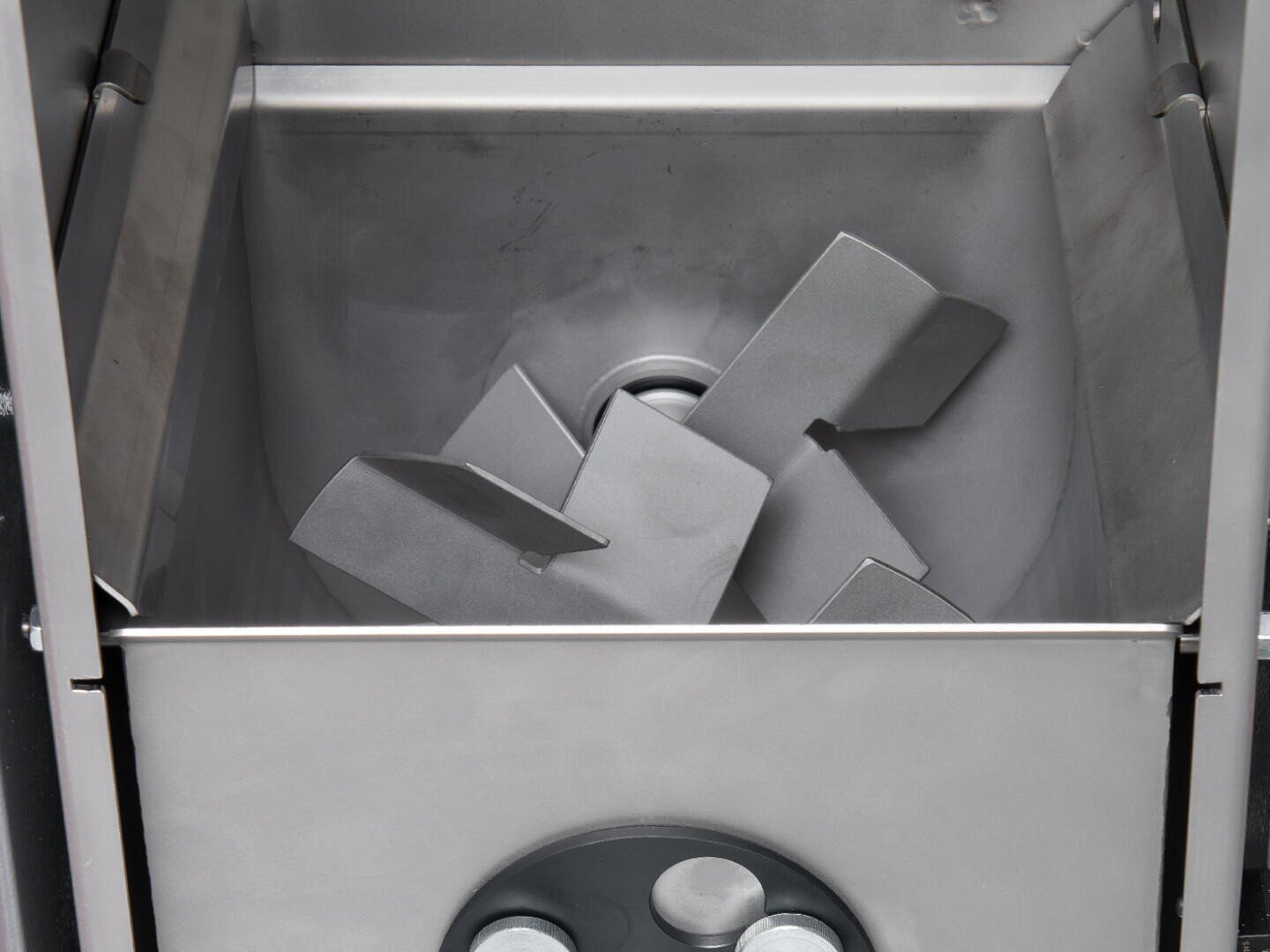 Gros plan sur l'intérieur d'une machine industrielle de mélange de métaux, avec des lames métalliques coudées dans une chambre rectangulaire.