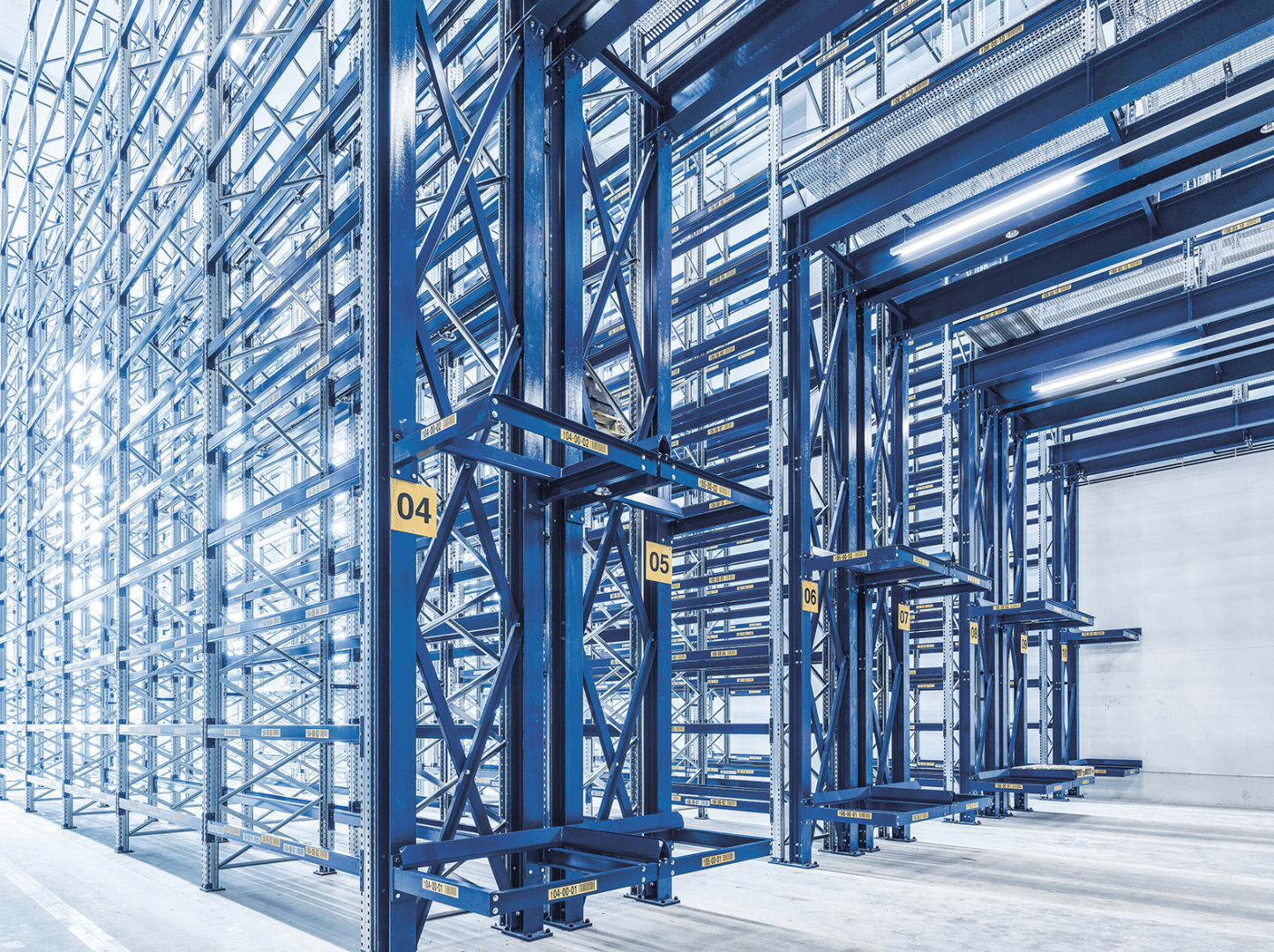 Großes, leeres Lagerhaus mit blauen Metallregalen, nummerierten Abschnitten und heller Beleuchtung, das einen industriellen Lagerbereich zeigt, der für die Inventur bereit ist.