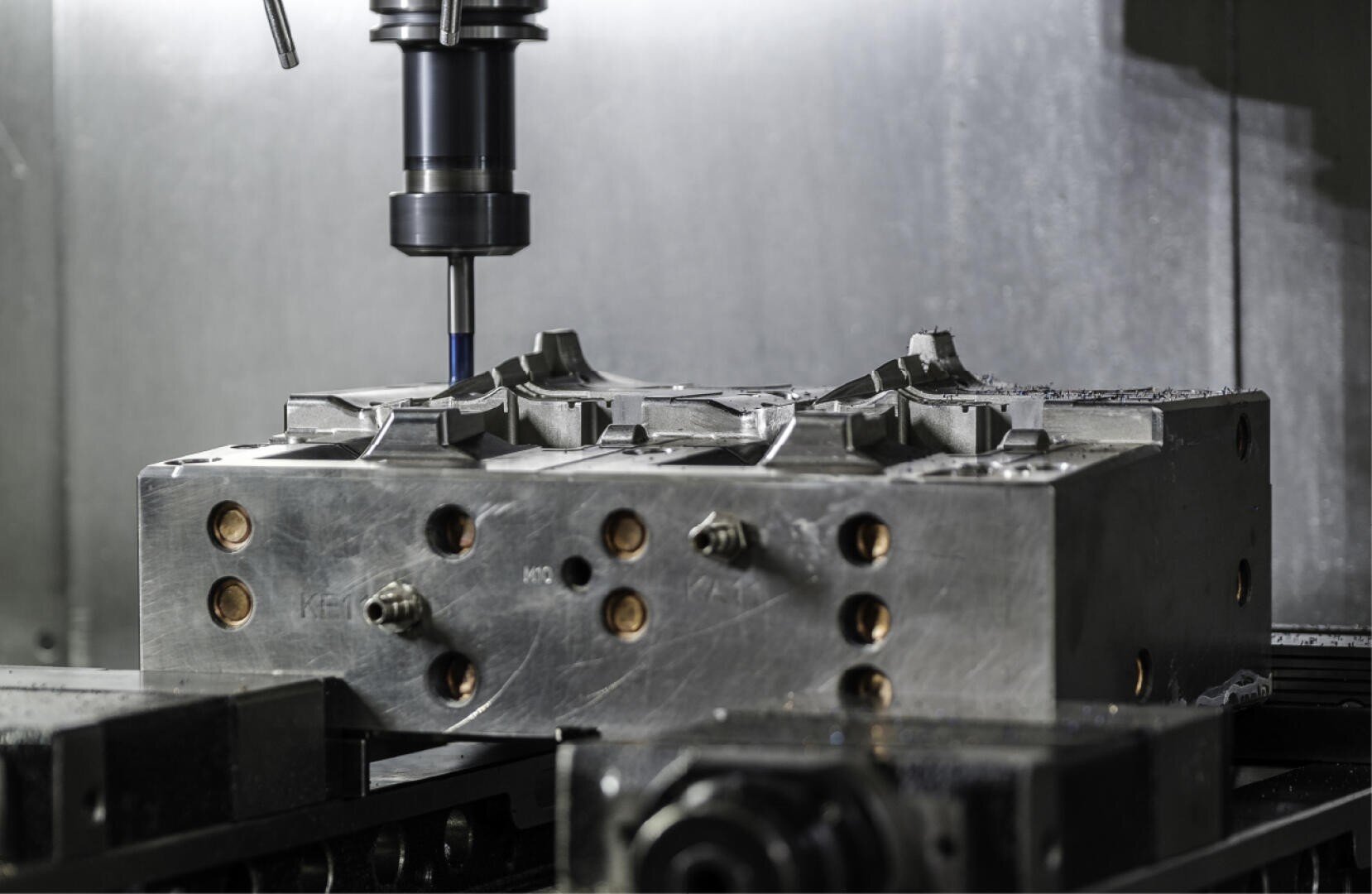 Gros plan sur une fraiseuse CNC découpant une forme métallique, l'outil de coupe se trouvant au-dessus de la surface détaillée et partiellement usinée. L'environnement est métallique et industriel.