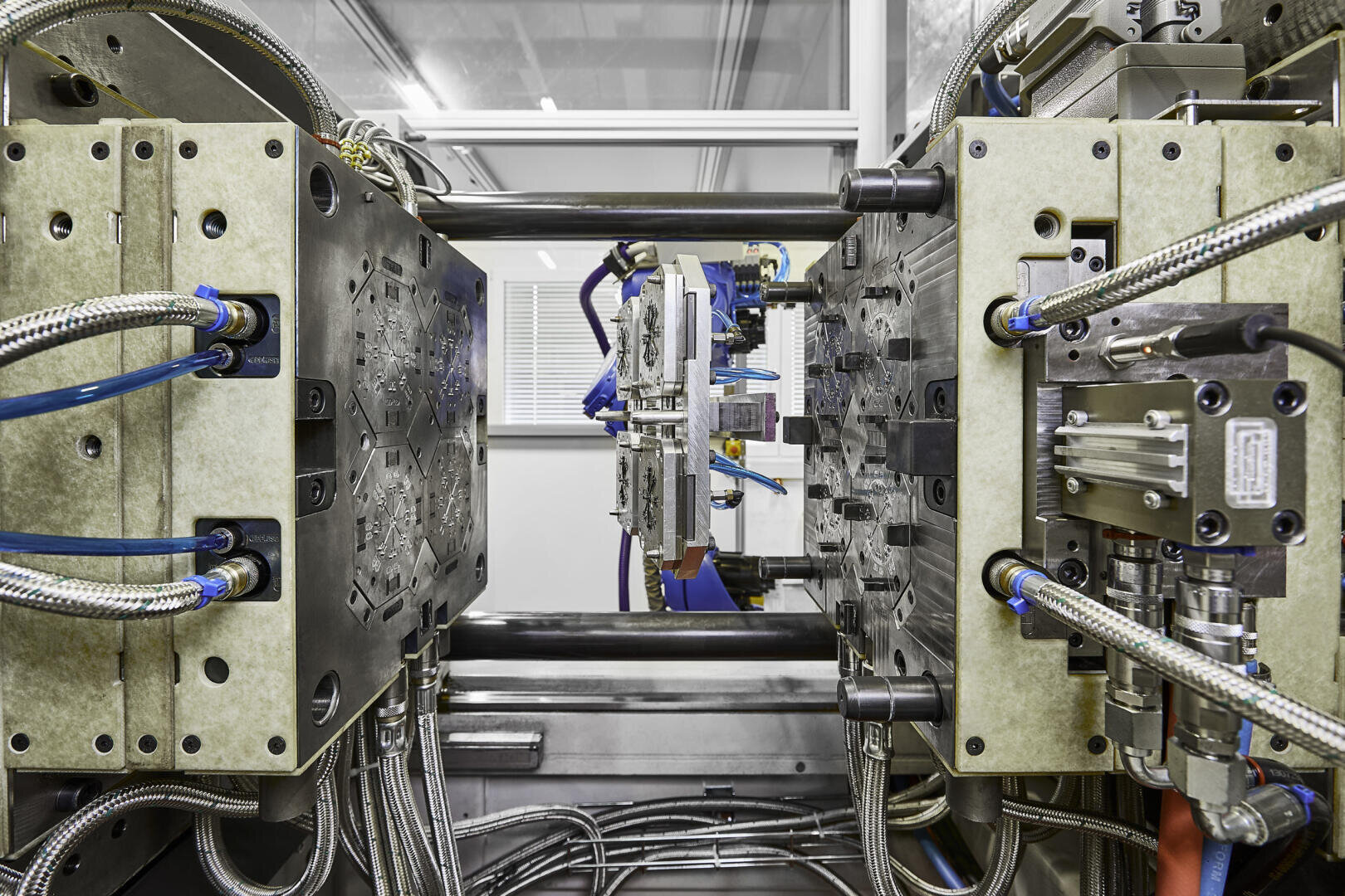 Gros plan sur une machine de moulage par injection industrielle avec des composants de moule métalliques détaillés, des tuyaux bleus et argentés et diverses pièces mécaniques dans une installation de production.