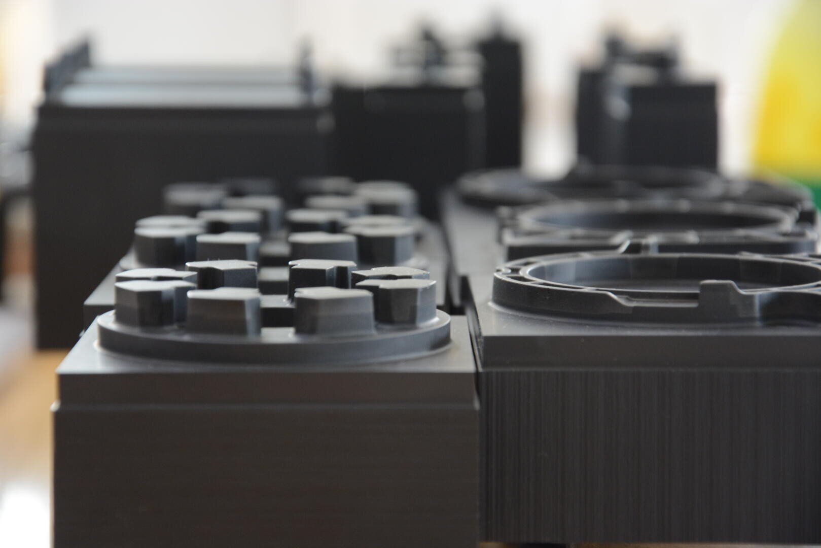 Gros plan sur de grands blocs en plastique noir avec des détails circulaires et rectangulaires, ressemblant à des briques de construction surdimensionnées, disposés en rangées sur un arrière-plan flou.