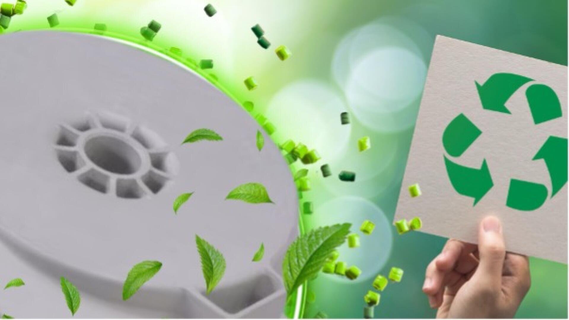 Eine Hand hält eine Karte mit einem grünen Recycling-Symbol. In der Nähe ist eine große Spule oder ein industrielles Bauteil von schwimmenden grünen Blättern und kleinen grünen Würfeln umgeben, die auf die Themen Recycling und Nachhaltigkeit hinweisen.