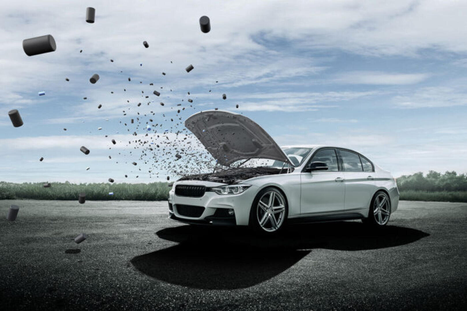 Ein weißes Auto mit geöffneter Motorhaube steht auf einer Straße. Motorteile scheinen als kleine Trümmer und Komponenten herauszufliegen, was vor dem bewölkten Himmel einen surrealen Effekt erzeugt.