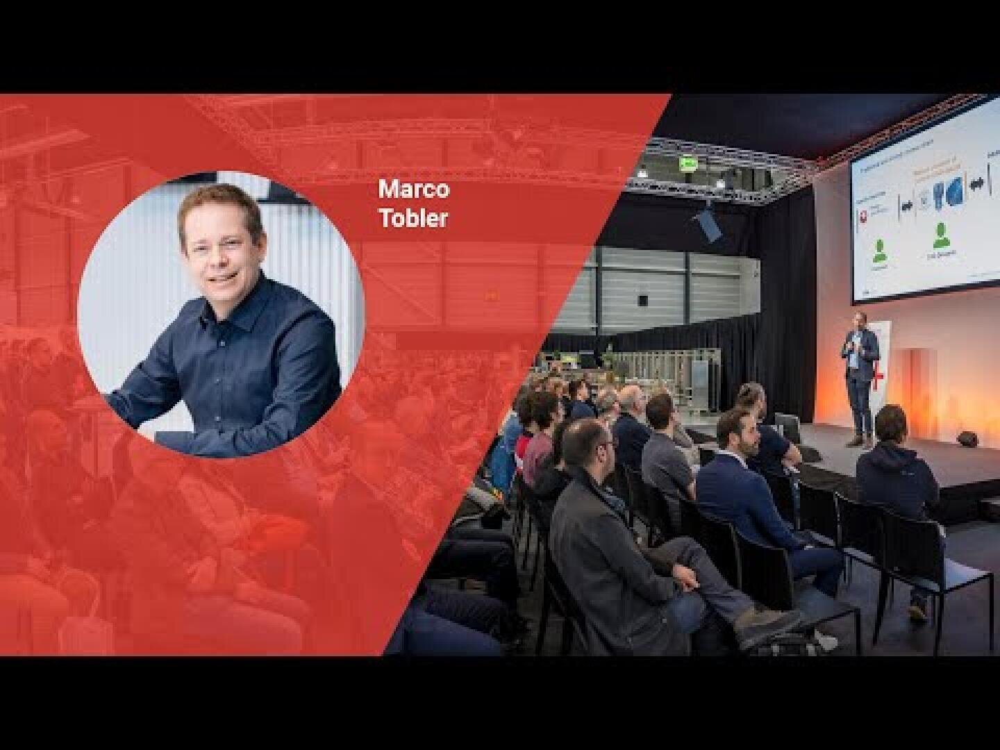 Eine Konferenzszene mit einer Menschenmenge, die vor einer Bühne sitzt, auf der ein Redner spricht. Auf der linken Seite ist in roter Farbe das Porträt eines lächelnden Mannes mit der Aufschrift Marco Tobler eingeblendet.