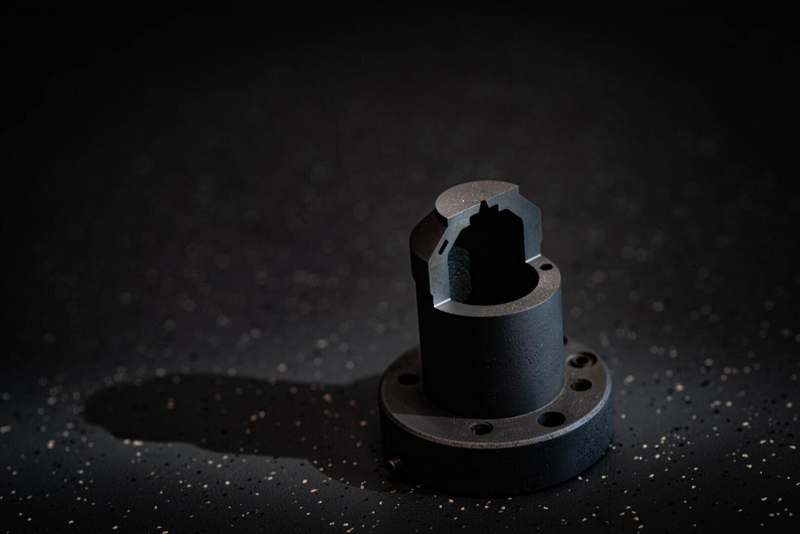 Un gros plan d'une pièce mécanique métallique cylindrique sombre avec un fond bridé et une découpe sur un fond sombre moucheté avec un éclairage et des ombres dramatiques.