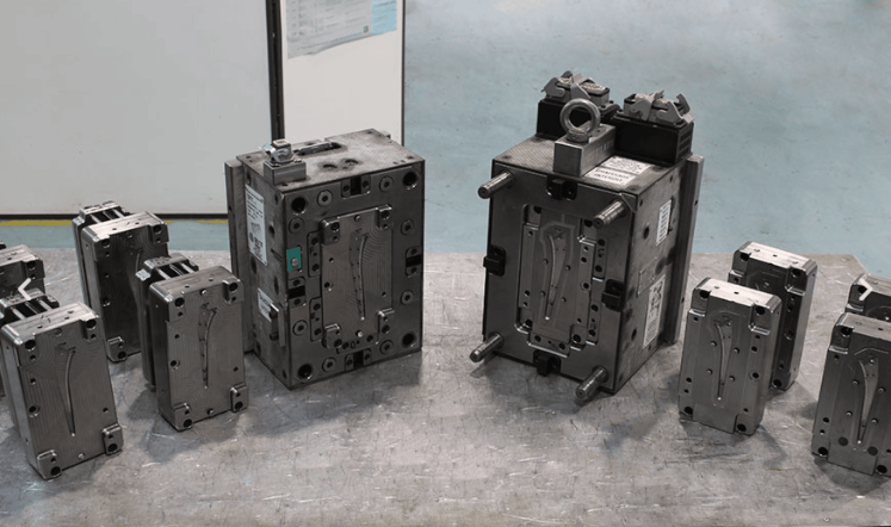 Mehrere Metallspritzgussformen unterschiedlicher Größe sind auf einem Werkstatttisch angeordnet, mit zwei größeren Formen in der Mitte und kleineren Formen auf beiden Seiten. Im Hintergrund sind Industriewände und -geräte zu sehen.