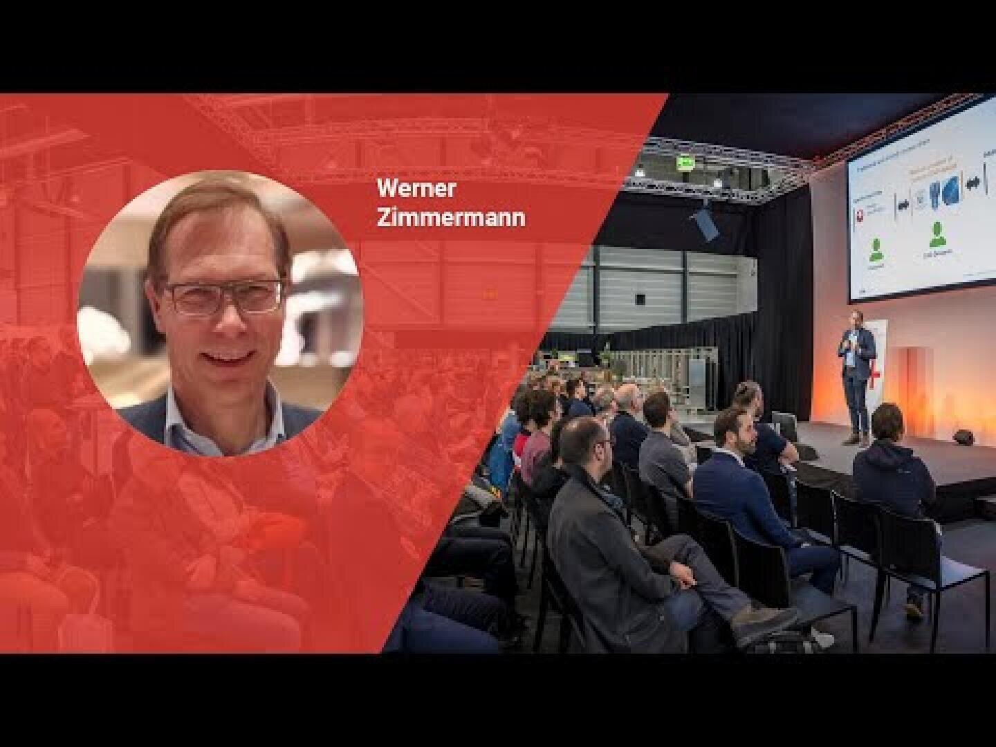 Ein Mann namens Werner Zimmermann ist in einem kreisförmigen Einschub auf einem roten Overlay zu sehen, während das Publikum einem Redner zuhört, der auf der Bühne eines Konferenzsaals Folien präsentiert.