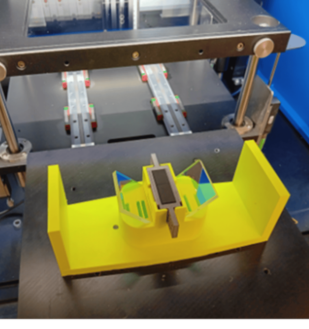 Eine Nahaufnahme eines 3D-Druckers in Betrieb, der ein gelbes Objekt mit eckigen Merkmalen druckt. Die Schienen und Mechanismen des Druckers sind im Hintergrund zu sehen.