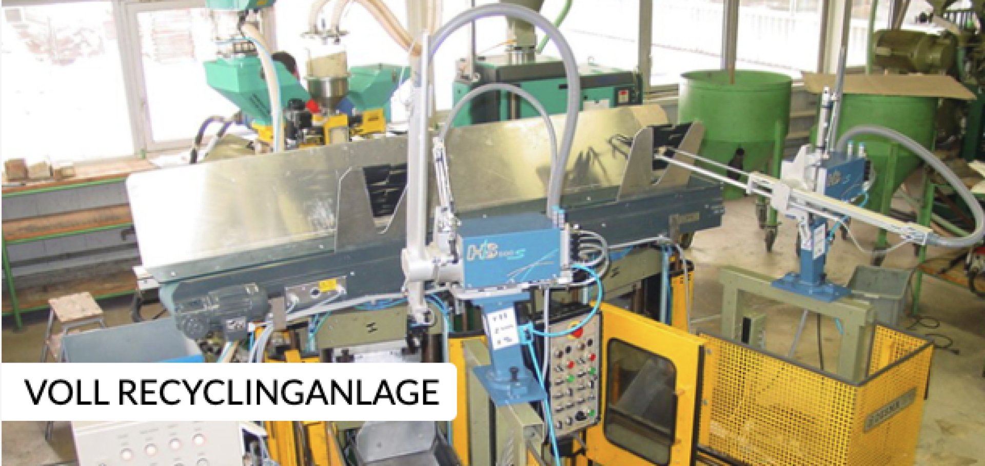 Blick auf eine automatisierte Recyclinganlage mit verschiedenen Maschinen, Schalttafeln und Rohren. Die Anlage wirkt sauber und modern. Auf einem Schild in deutscher Sprache steht VOLL RECYCLINGANLAGE, d. h. eine komplette Recyclinganlage.