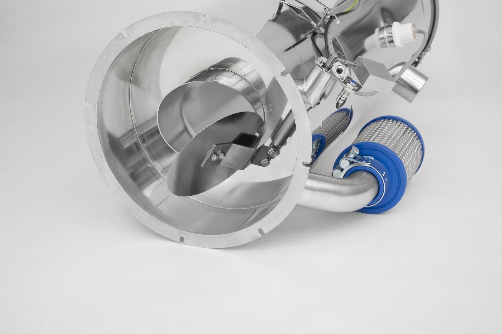 Eine Nahaufnahme eines industriellen Bauteils aus glänzendem Edelstahl mit einer großen kreisförmigen Öffnung, abgewinkelten Metallblättern im Inneren und blau abgedeckten Filterelementen, die an gebogenen Rohren befestigt sind.