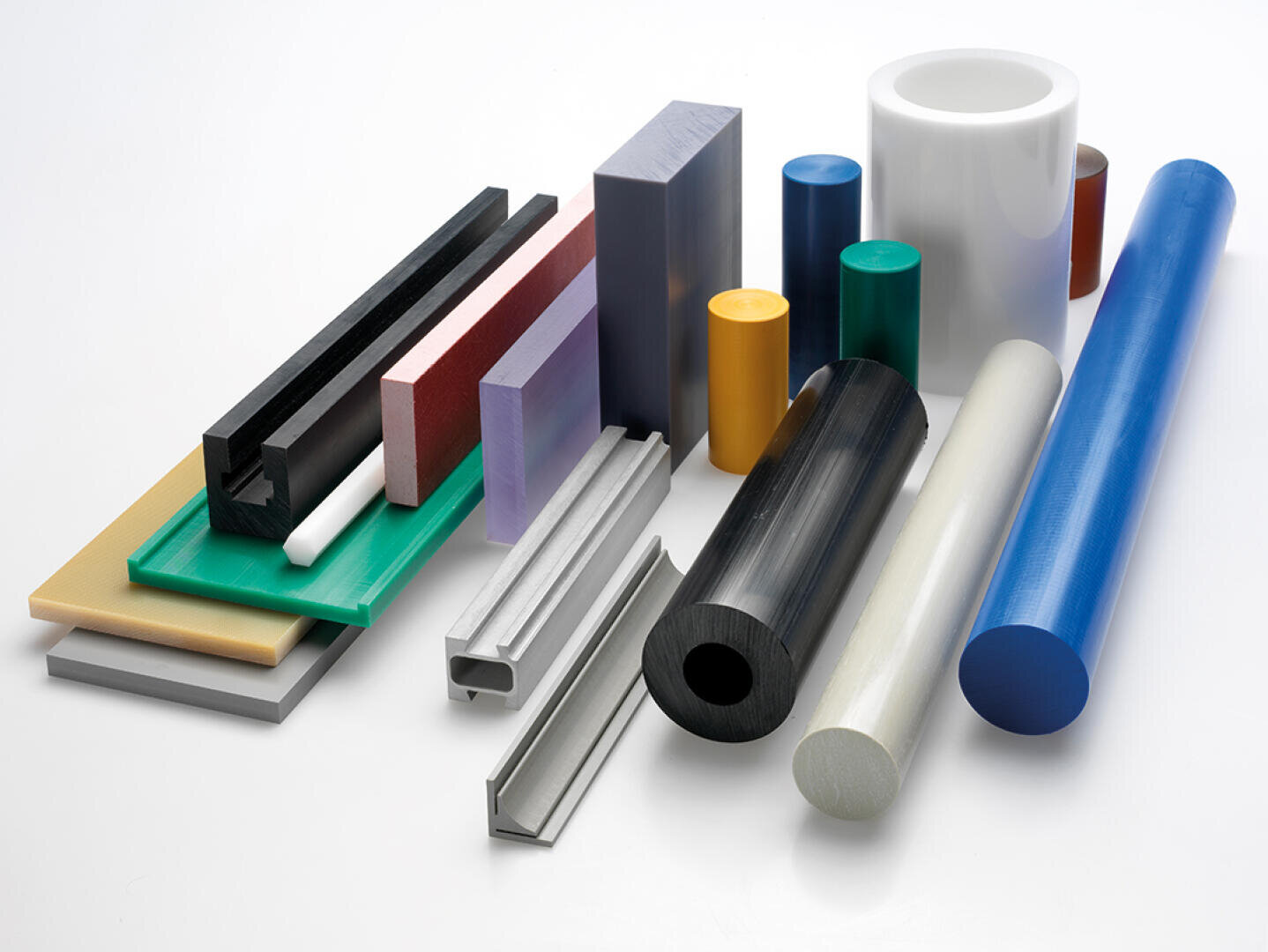 Ein Sortiment von Kunststoffstäben, -rohren und -platten in verschiedenen Farben und Größen, die auf einem weißen Hintergrund angeordnet sind. Zu den Formen gehören Zylinder, rechteckige Blöcke und Kanäle.
