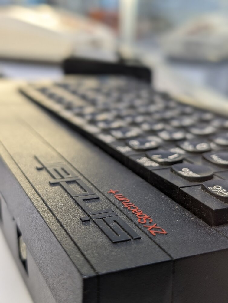 Nahaufnahme eines schwarzen ZX Spectrum+2 Vintage-Computers, der die Tastatur und die Aufschrift ZX Spectrum+2 in roter Schrift zeigt. Der Fokus liegt auf dem Schriftzug, während die Tasten im Hintergrund leicht verschwommen sind.